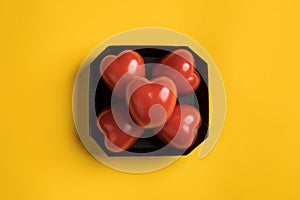 Red tomatoes in the form of a heart in a black cardboard box, on a yellow background. Healthy food concept. Top view.