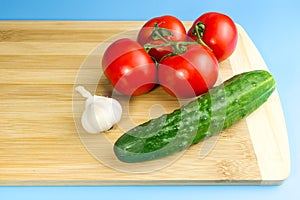 Red tomatoes, green cucumber, garlic on a wooden board