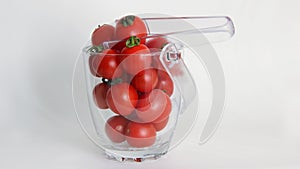 red tomatoes with green tails in a glass vase on a white background