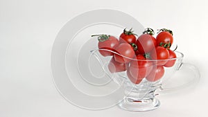 Red tomatoes with green tails in a glass vase on a white background close up