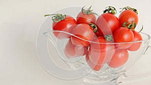 Red tomatoes with green tails in a glass vase on a white background close up