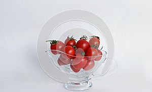 Red tomatoes with green tails in a glass vase on a white background close up