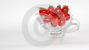 Red tomatoes with green tails in a glass vase on a white background close up