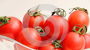 Red tomatoes with green tails in a glass vase on a white background close up