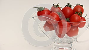 Red tomatoes with green tails in a glass vase on a white background close up