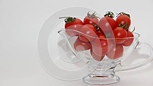 Red tomatoes with green tails in a glass vase on a white background close up