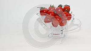 Red tomatoes with green tails in a glass vase on a white background close up