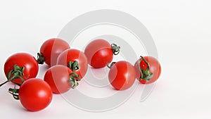 Red tomatoes with green tails in a glass vase on a white background close upsmall red Cheri tomatoes with green tails lie scattere