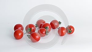 Red tomatoes with green tails in a glass vase on a white background close upsmall red Cheri tomatoes with green tails lie scattere