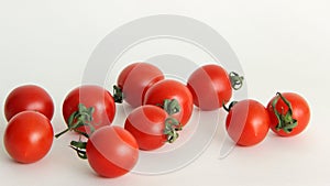 Red tomatoes with green tails in a glass vase on a white background close upsmall red Cheri tomatoes with green tails lie scattere