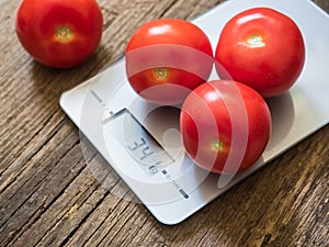 Red tomatoes on kitchen scale on wooden background. Product weighing