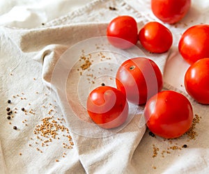 Red tomatoes on a linen towel. In the folds of the fabric of the moaning pepper and mustard in the grains.