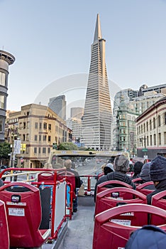 Red tourist bus riding in San Francisco under a blue sky with modern skyscrapers around it