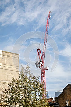 Red Tower Crane Above Buildings and Trees Under a Blue Cloudy Sky