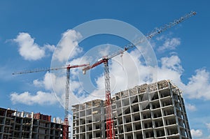 Red tower cranes standing on construction site unfurling their jibs over gray frames of block apartment buildings