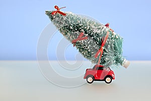 Red toy car carrying a Christmas tree on blue background. Space for text