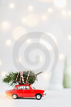 Red toy car with a christmas tree on the roof, garland bokeh on background, vertical orientation