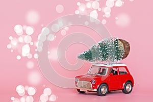 Red toy car with a christmas tree on the roof on pink paper background. Winter delivery, xmas, happy new year 2020 celebration