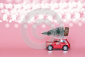 Red toy car with a christmas tree on the roof on pink paper background. Winter delivery, xmas, happy new year 2020 celebration