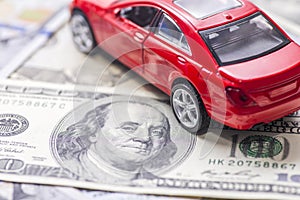 Red toy car on dollar bills. Cost of buying a car, fuel, insurance and other car costs