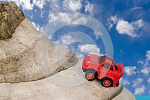 Red toy car driving up a mountain Blue sky with clouds