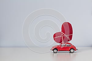 Red toy retro car carries a red plush heart on the roof