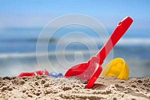 red toy shovel and plastic molds in the sand at the beach, concept of summer vacation with children at sea, copy space