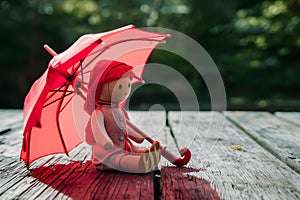 Red toy umbrella next to wooden doll, travel whimsy