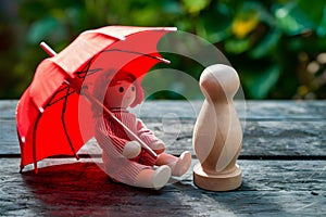 Red toy umbrella next to wooden doll, travel whimsy