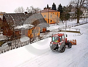 A red tractor clears the road from the snow. Winter cleaning of the street. Community service. Weather. Winter village. Snowblower