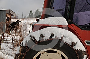A red tractor beside a cow and barn in the snow