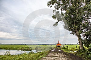 Red tractor drives through a gate next to a creek into field, agricultural transport, with a cloudy sky background