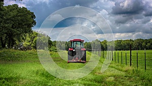 Red tractor mowing grass under rainy sky