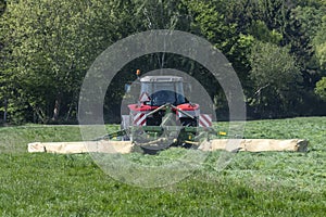 Red tractor mowing tall green grass