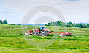 A red tractor mows the grass on a farmer's field. Two mowers will mow a large area of the field.