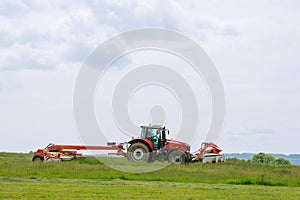 A red tractor mows the grass on a farmer's field. Two mowers will mow a large area of the field.