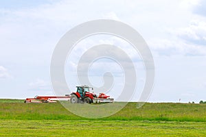 A red tractor mows the grass on a farmer's field. Two mowers will mow a large area of the field.