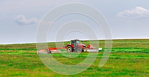 A red tractor mows the grass on a farmer's field. Two mowers will mow a large area of the field.