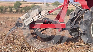 Red tractor with plough plowing field soil close up view in slow motion.