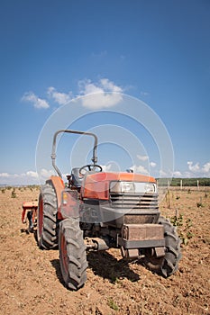 Red tractor with plow in field. Cloudy sky