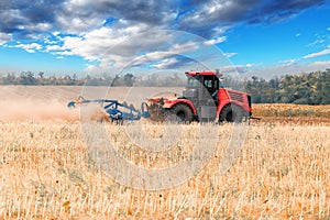 Red tractor plowing field, raising clouds of dust