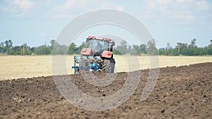 Red tractor plows the ground