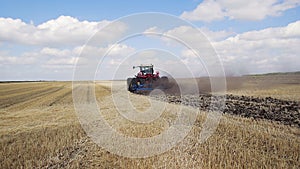 A red tractor with a reverse plow plows a field.