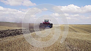 A red tractor with a reverse plow plows a field.