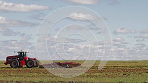 Red tractor with a reverse plow plows a field. A stork walks nearby and collects food. Agricultural work in the field