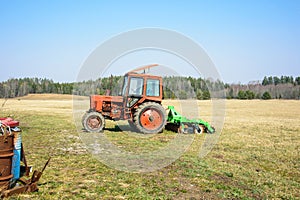 A red tractor stands on a field in early spring.
