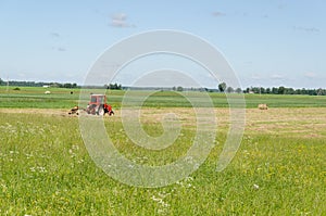 Red tractor ted hay dry grass in agriculture field