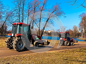 Red tractors trucks in spring city park. Cleaning. Early spring. Works. Sunny spring day.