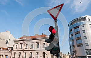 Red traffic light for vehicles and cars on the crosswalk on the street in the city close up with buildings and blue sky background