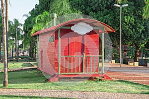 Red trailer through the park with old railway track, some benches and many trees and green nature around. Plate to put your